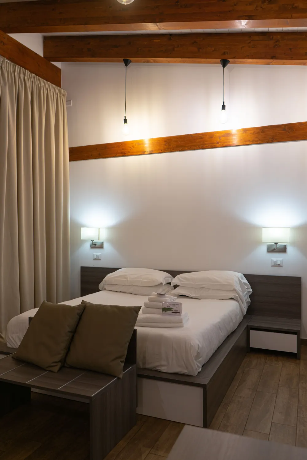 Camera matrimoniale con travi in legno a vista e asciugamani piegati sul letto